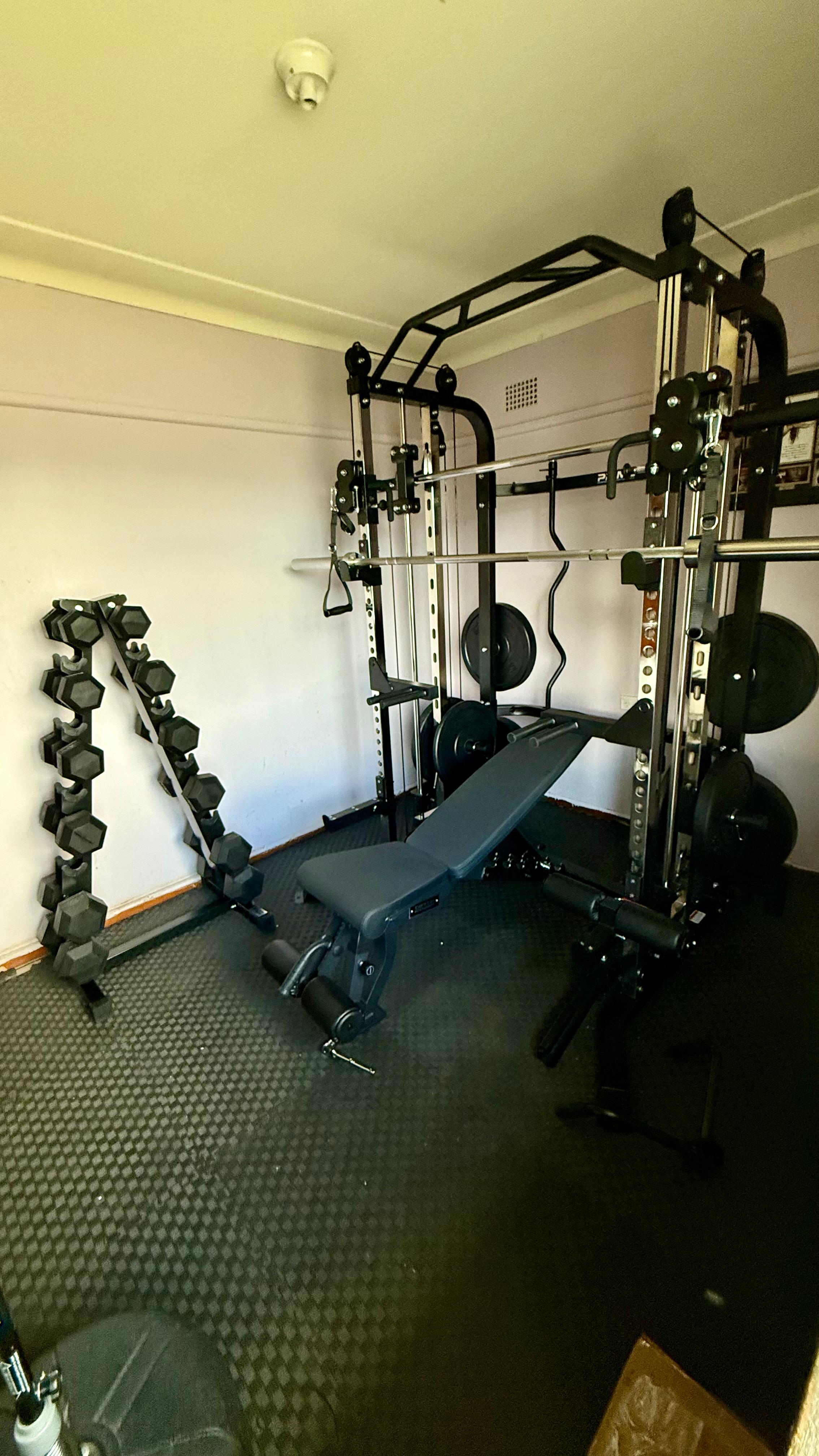 Client-assembled G3S functional smith machine set up in a home gym with bench, plates and dumbbells